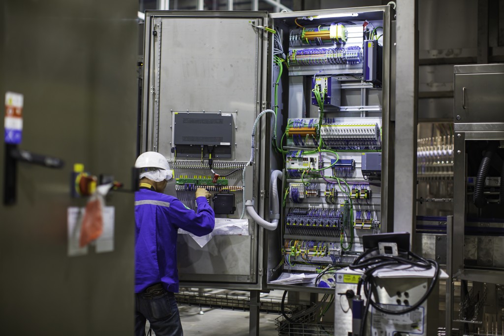 Elektrofachkraft prüft einen Schaltschrank in einer Fabrikhalle