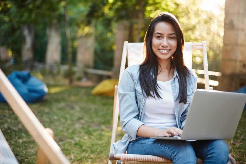 Ein englisches Fernstudium lässt sich auch aus dem Ausland absolvieren – sofern Prüfungen, Präsenztermine und Zeitzonen dazu passen. Frau arbeitet im Freien mit einem Laptop