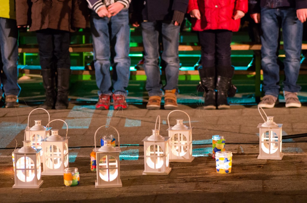 Menschen mit bunten Laternen auf einem Weg bei Dunkelheit