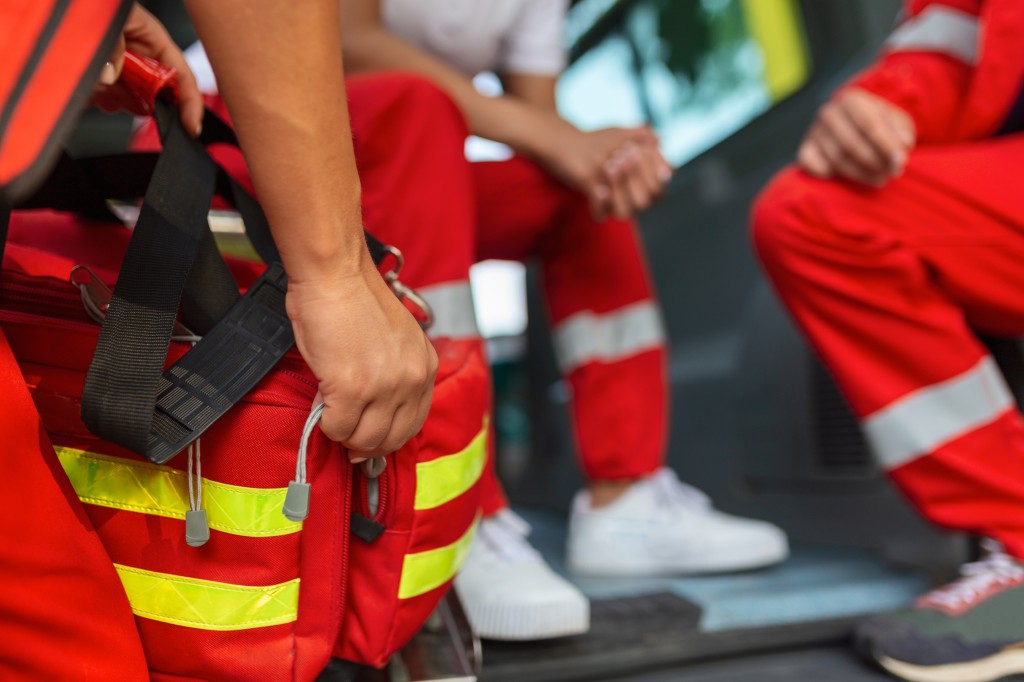 Rettungskraft in roter Einsatzkleidung richtet am Heck eines Rettungsfahrzeugs die Erste-Hilfe-Tasche für einen Einsatz her