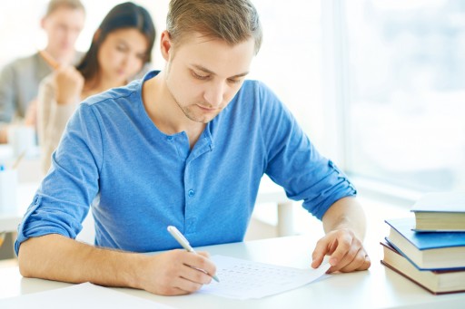 Junger Mann sitzt konzentriert mit Stift in einem Prüfungsraum
