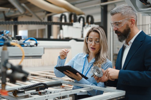 Ingenieurin und Projektleiter besprechen sich mit Tablet in einer Fertigungshalle
