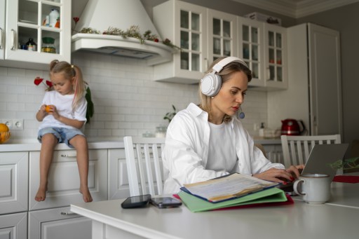 Mutter arbeitet am Küchentisch am Laptop, während ihr Kind neben ihr sitzt